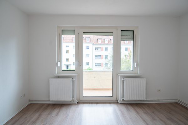 Das Wohnzimmer mit Zugang zum Balkon lädt mit dem hellen Laminat, frisch gestrichenen Heizkörpern und Wänden zum Wohlfühlen ein.
